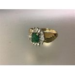 An emerald and diamond cluster ring, the central baguette-cut emerald claw-set within a sunburst