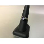 An amethyst and diamond ring, the central oval-cut amethyst claw-set between shoulders each with a