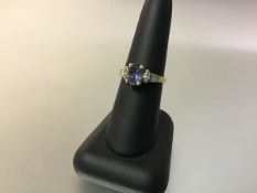 An amethyst and diamond ring, the central oval-cut amethyst claw-set between shoulders each with a