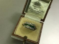 An emerald and diamond cluster ring, c. 1930, with a row of calibre-cut emeralds flanked by twin
