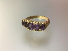 A five stone amethyst ring, the graduated oval-cut stones on a scroll-cast and engraved mount, on an