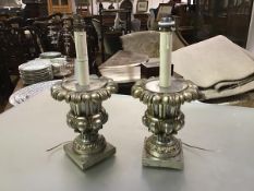 A pair of silvered wooden urn form table lamps, each boldly modelled on a square base with faux-