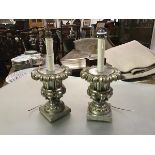 A pair of silvered wooden urn form table lamps, each boldly modelled on a square base with faux-