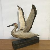 A hand-made and painted wooden model of a bird, modelled with outstretched wings, on an ebonised