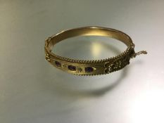 A late Victorian ruby and diamond set 9ct gold bangle, hinged, mounted with three oval-cut rubies