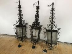 A set of three large wrought-iron lanterns, the cylindrical frames with pierced mounts and scrolling