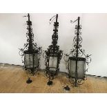 A set of three large wrought-iron lanterns, the cylindrical frames with pierced mounts and scrolling