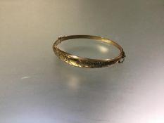 A 9ct yellow gold bangle, hinged, the hollow tapering band scroll-engraved, hallmarked for Chester