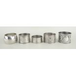 FOUR SILVER NAPKIN RINGS OF VARIOUS DESIGN together with one white metal napkin ring, 118 grams