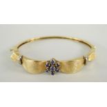 14CT YELLOW GOLD BANGLE with seven-stone sapphire cluster and diamond chip decoration, 17.2grams