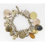 9CT YELLOW GOLD CURB LINK CHARM BRACELET HAVING HEART SHAPED PADLOCK and assorted coins and charms