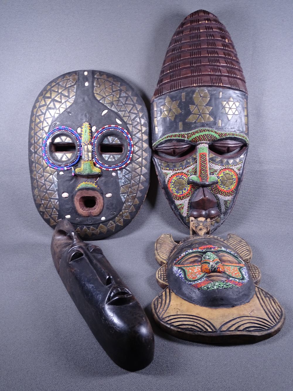 FOUR CARVED TRIBAL WALL MASKS, the majority having colourful beadwork decoration