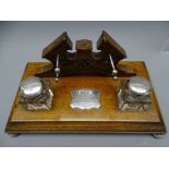 DESK INKSTAND, oblong oak on corner ball feet with carved pen stand and pair of plain square glass