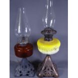 TWO IRON BASED OIL LAMPS, one with a cranberry reservoir and another with a milk glass yellow