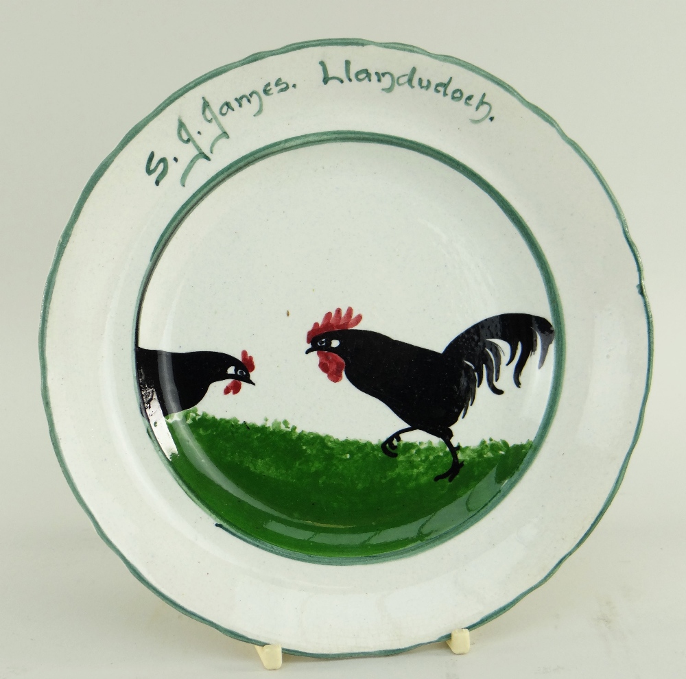 LLANELLY POTTERY TEA PLATE PAINTED WITH TWO STRUTTING BLACK COCKS inscribed to border S J James,