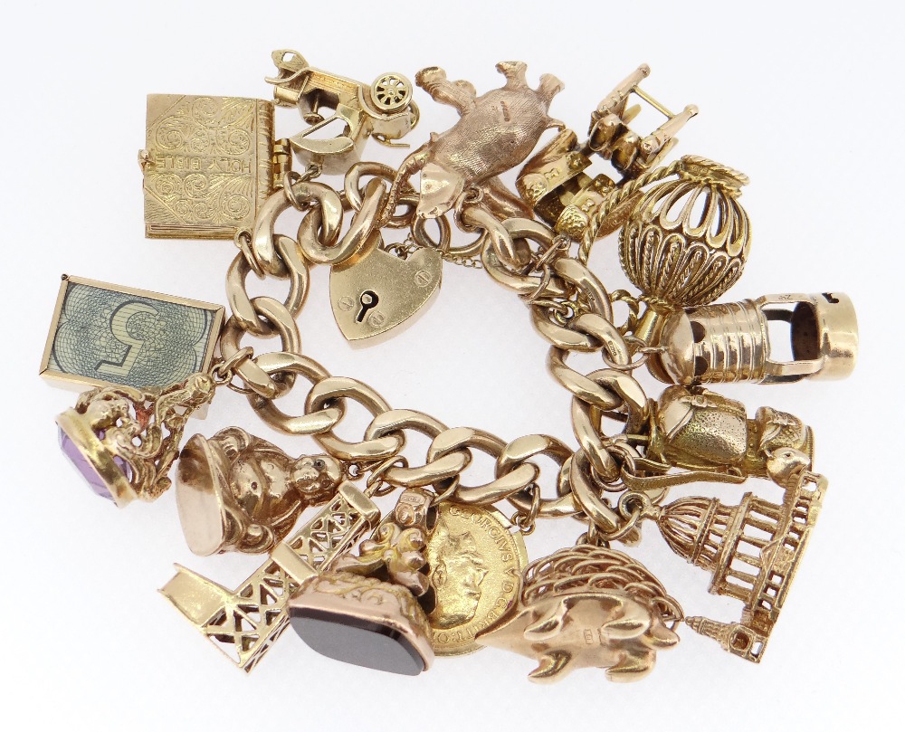 HEAVY 9CT GOLD FLAT CURB LINK CHARM BRACELET having an assortment of mainly 9ct gold charms