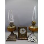 TWO VINTAGE GLASS FONT OIL LAMPS on cast iron bases and a wooden cased mantel clock