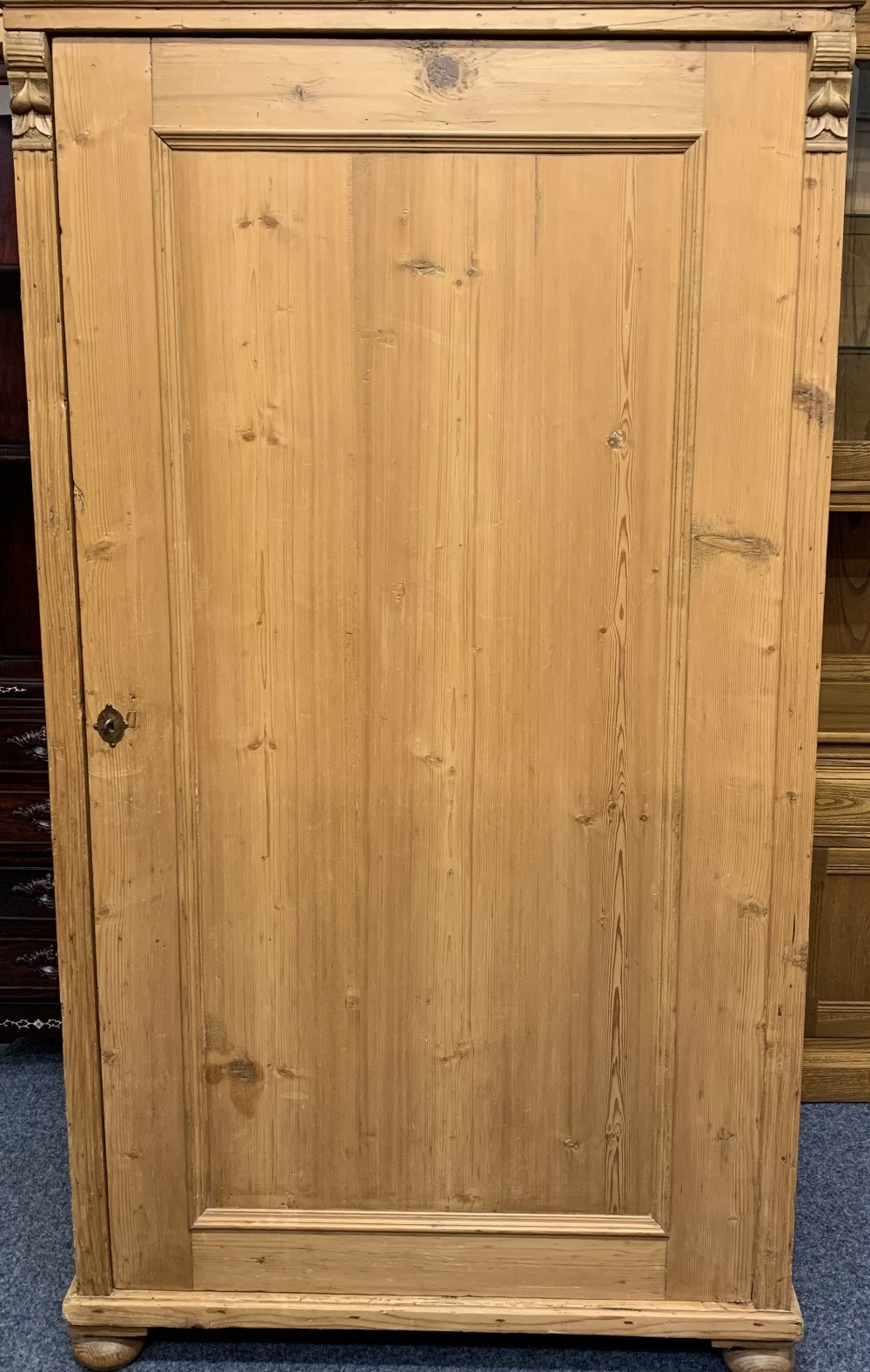 CONTINENTAL STRIPPED PINE SINGLE DOOR WARDROBE with carved detail to the front on turned bun feet,