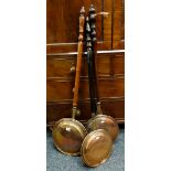 THREE VICTORIAN COPPER WARMING PANS with turned handles, all with foliate decorated covers,