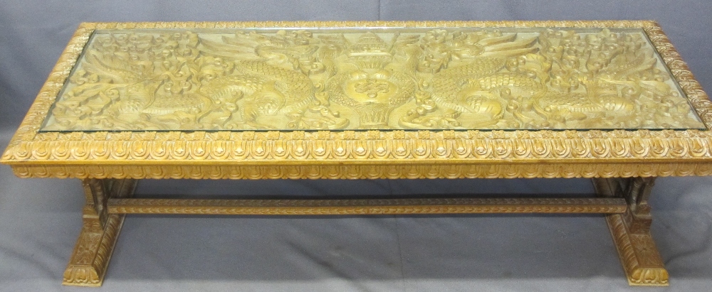 AN EASTERN HEAVILY CARVED LONG-JOHN COFFEE TABLE with a glazed top, 50cms H, 150cms W, 56cms D