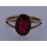 A BELIEVED GOLD (UNMARKED) RING with an oval ruby on split shoulders, 2.5grms, size N/O