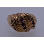 A 9CT GOLD DRESS RING with three rows of tiny rubies in a wavy style setting, 5grms, size O
