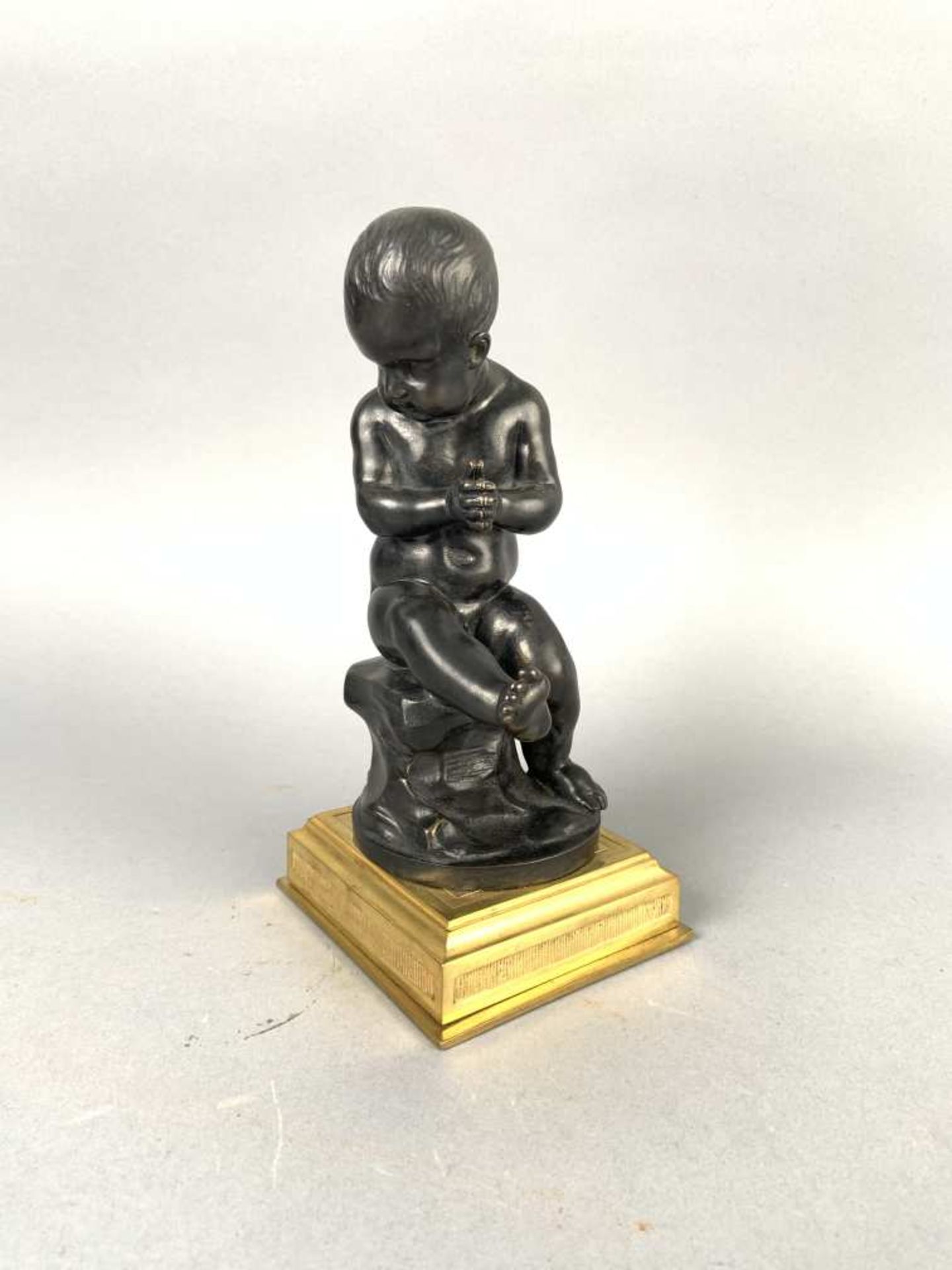 Chérubin assis sur un rocher. Bronze sur socle de laiton. H. 19 cm.