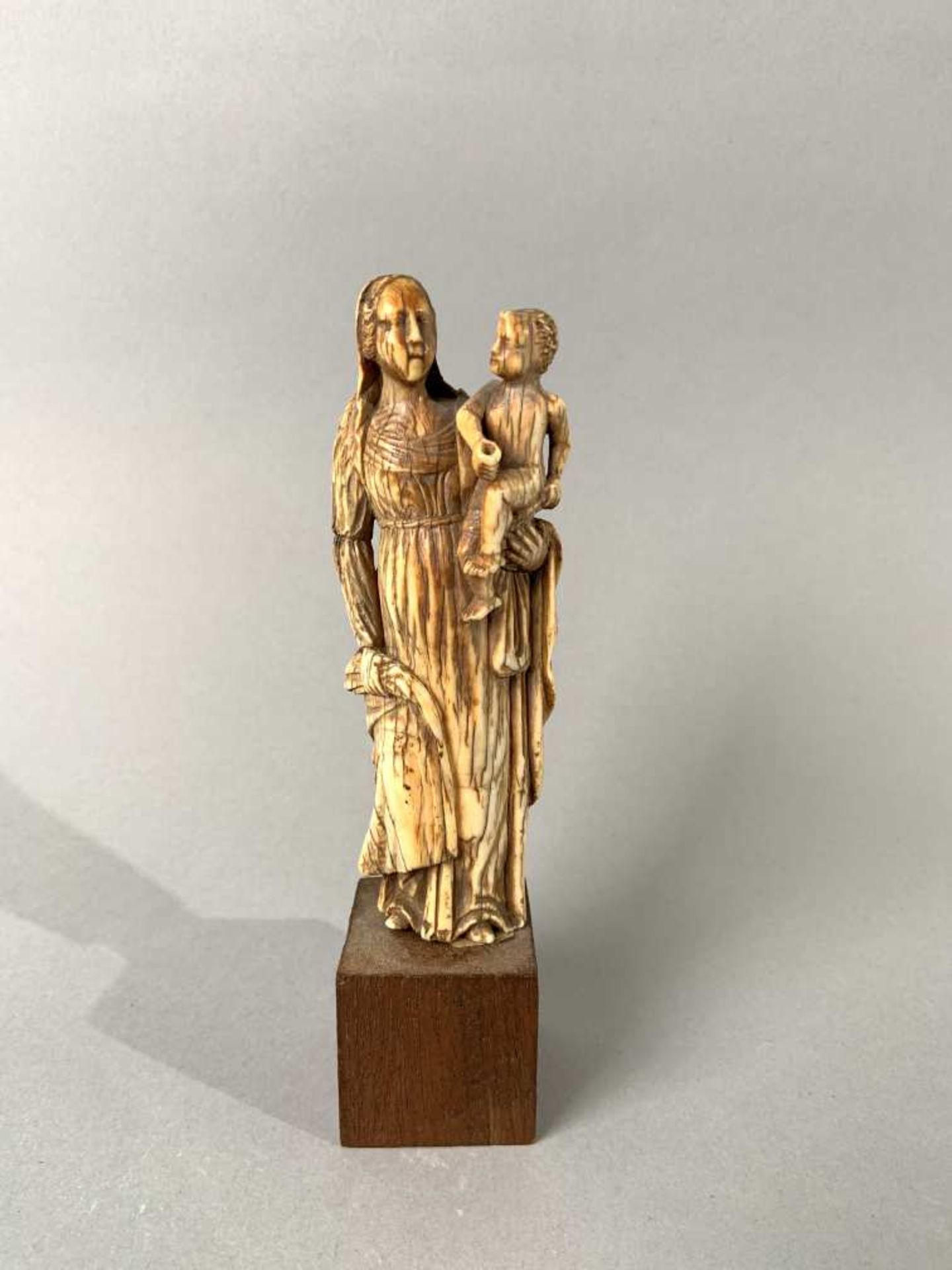 Vierge à l'Enfant en ivoire sculpté en ronde-bosse, patine brune. Debout, Marie porte l'Enfant sur