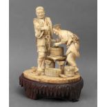 19th century Japanese school. A carved ivory okimono depicting two characters milling grain