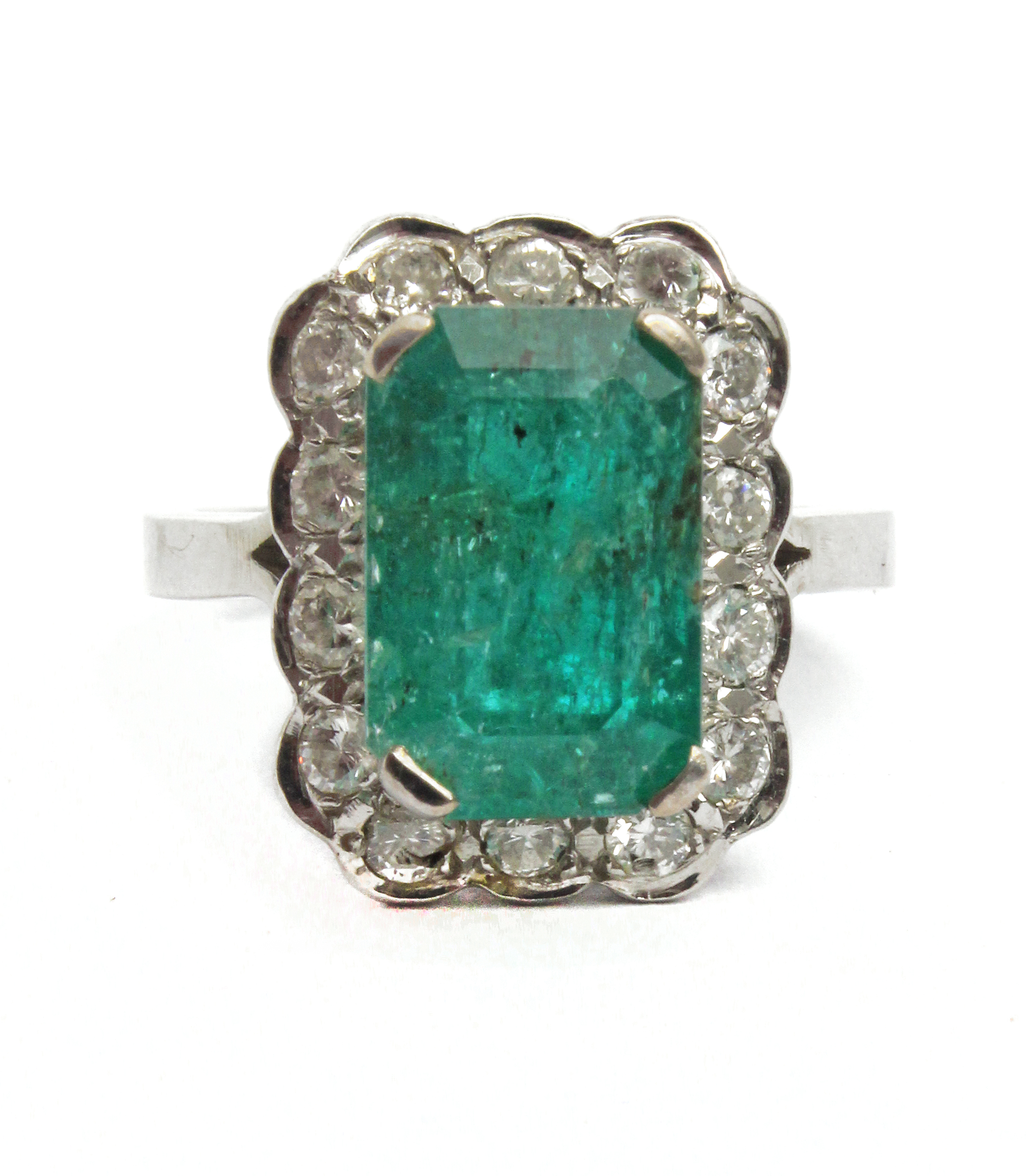 An emerald and diamonds cluster ring with an 18k. white gold setting