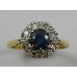 An 18ct gold sapphire and diamond cluster ring, claw set with a mixed cut stone, bordered by