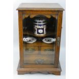 An Edwardian oak smokers cabinet, the glazed door opening to reveal a tobacco jar (A/F), two ash