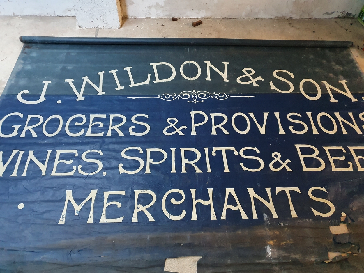 An Edwardian blue canvas roller shop banner, white painted "J. Wildon & Sons.....", 220 x 355 cm