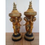 A pair of gilt and black painted resin garnitures, depicting cherubs holding lidded bowls 30 cm.