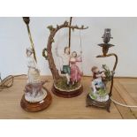 A table lamp with a bisque model of a boy and girl on a swing, and two other figural table lamps,