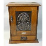 An Edwardian Art Nouveau smokers cabinet, the ebmossed copper floral panel door opening to reveal