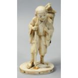 A Japanese Meiji period Ivory Okimono, carved to depict a travelling scribe, his back pack with