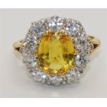 An 18 ct gold yellow sapphire and diamond cluster ring, claw set with an oval mixed cut stone,