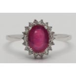 A 9k white gold, ruby and diamond cluster ring, claw set with a mixed cut stone, bordered by rose