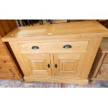 A solid oak side cabinet of panel construction, single frieze drawer over two cupboard doors,