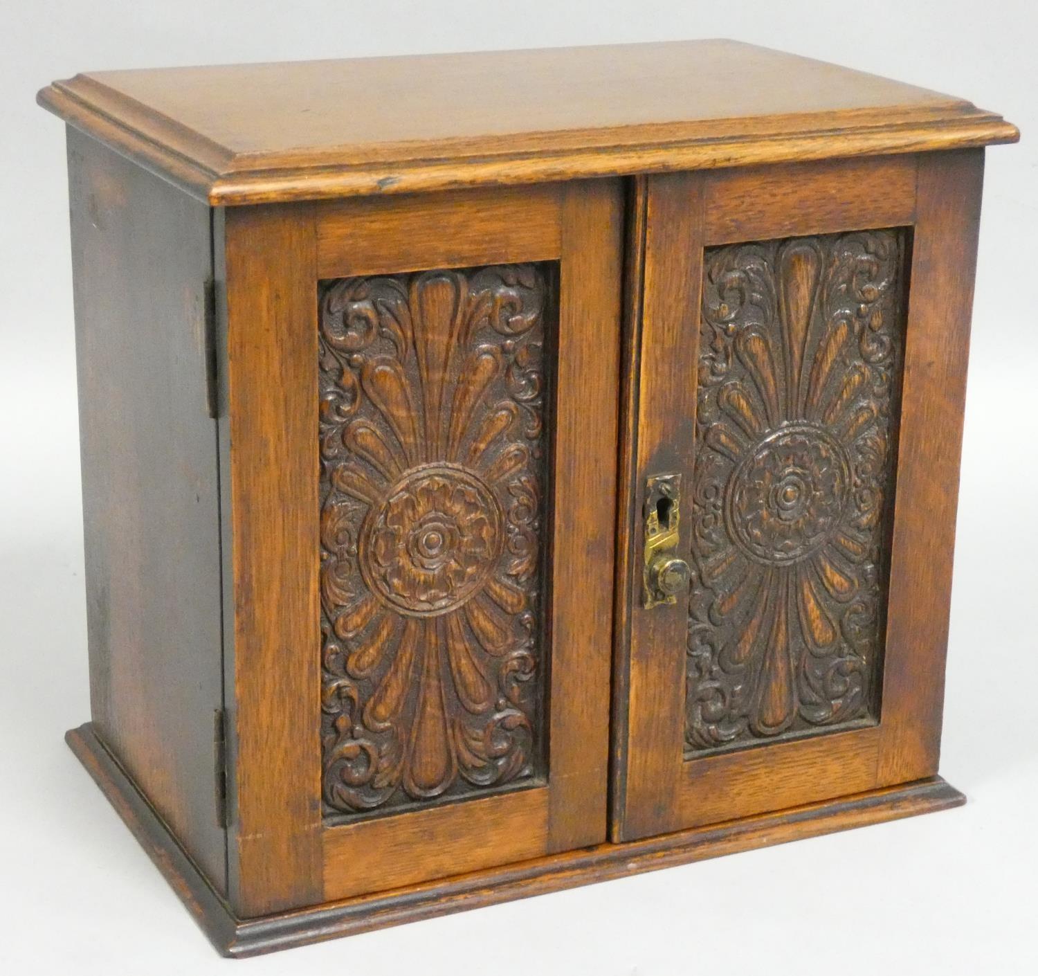 An Edwardian oak smokers cabinet, the panel doors carved with floral decoration, opening to reveal