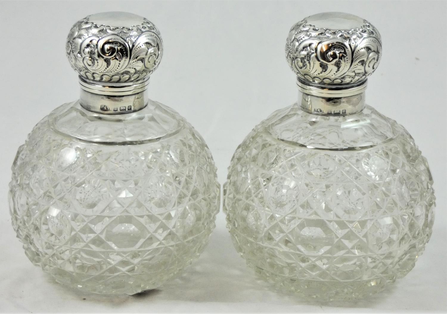 A pair of silver capped cut glass scent bottles, Birmingham 1904, the embossed hinged covers (one