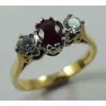 An 18ct gold ruby and diamond three stone ring, claw set with an oval mixed cut stone flanked by