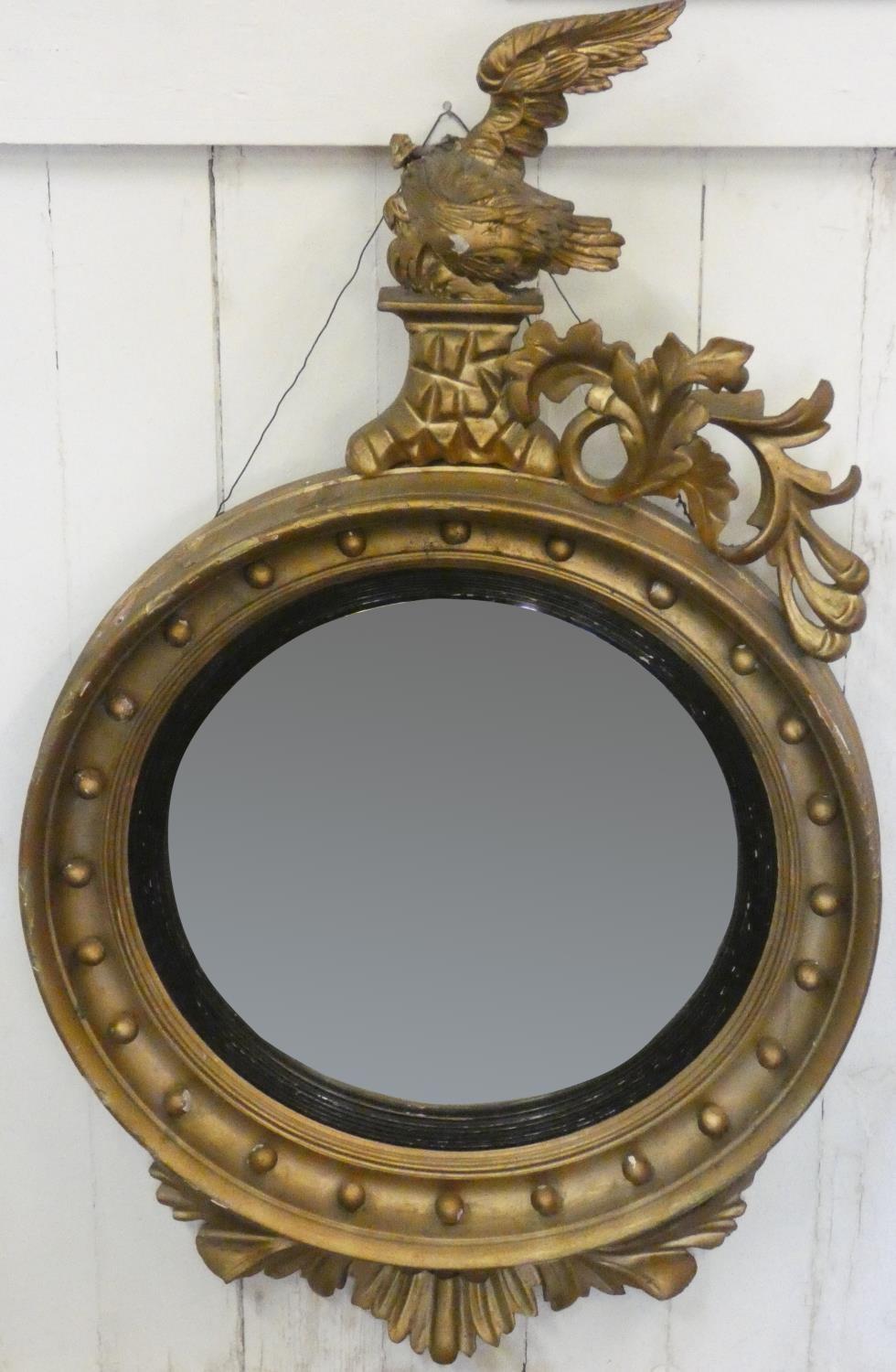 A giltwood convex circular wall mirror, with eagle and floral scroll surmount, A/F, 108 cm.