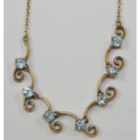 A 9ct gold a blue zircon necklace, composed of seven brilliant cut stones in a scroll front setting,