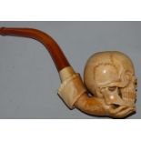 A Victorian meerschaum pipe, carved in the form of a skull held by a hand, 17 cm.