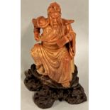 A Chinese soapstone figure of a seated man reading a book, Qing dynasty, raised on a brown hardstone