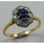An 18ct gold sapphire and diamond cluster ring, claw set with an oval mixed cut stone, bordered by