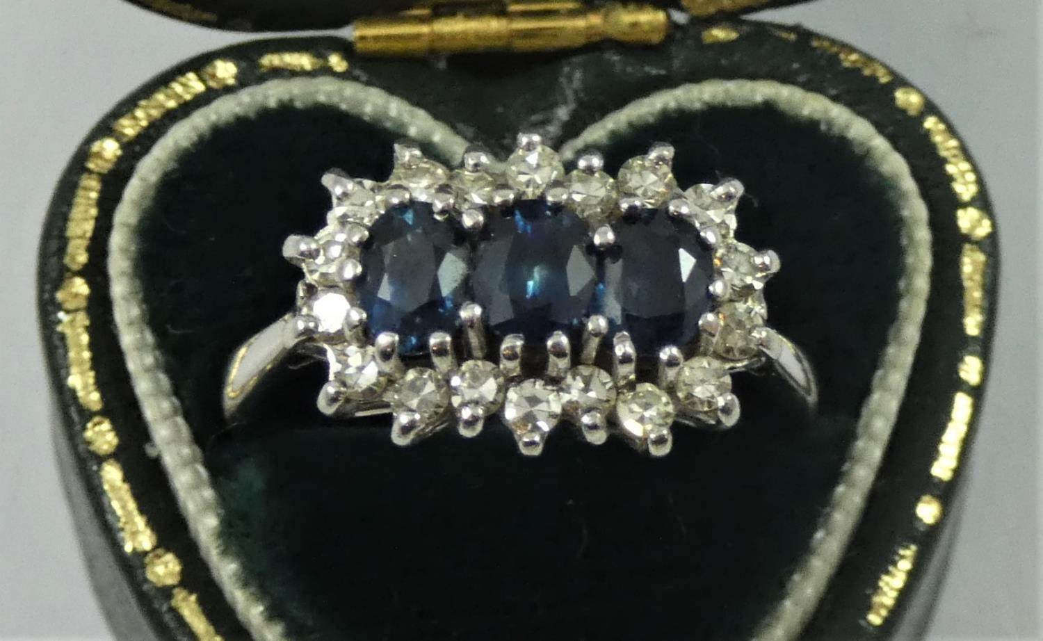 An 18ct white gold sapphire and diamond three stone ring, the oval mixed cut stones bordered by