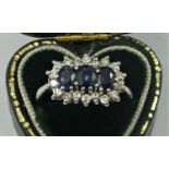 An 18ct white gold sapphire and diamond three stone ring, the oval mixed cut stones bordered by
